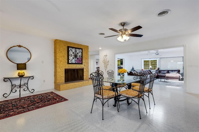 dining space with a stone fireplace and ceiling fan