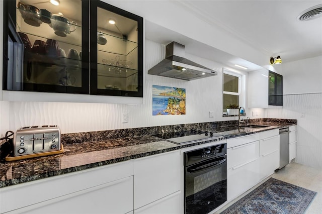 kitchen featuring dark stone counters, wall chimney exhaust hood, sink, black appliances, and white cabinetry