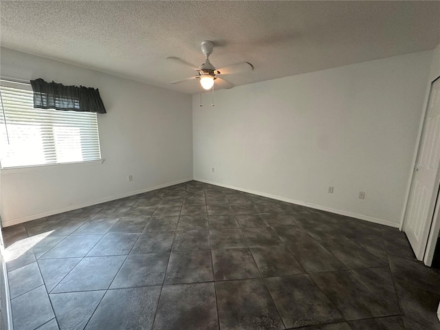 spare room featuring dark tile flooring, ceiling fan, and a textured ceiling