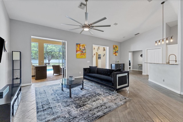 living room with hardwood / wood-style floors, ceiling fan, sink, and high vaulted ceiling