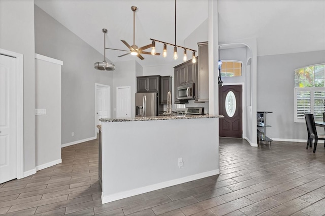 kitchen with high vaulted ceiling, hanging light fixtures, light stone countertops, appliances with stainless steel finishes, and dark hardwood / wood-style flooring