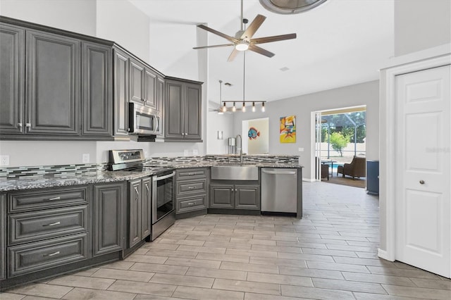 kitchen with a high ceiling, sink, light wood-type flooring, decorative light fixtures, and stainless steel appliances