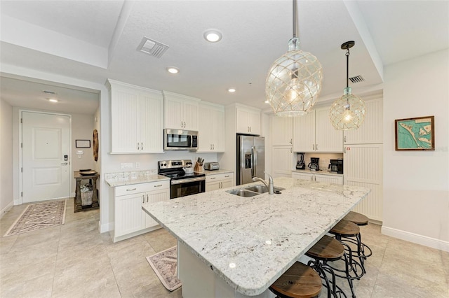 kitchen with stainless steel appliances, a kitchen island with sink, sink, a breakfast bar, and pendant lighting