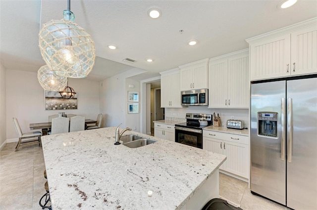 kitchen featuring appliances with stainless steel finishes, hanging light fixtures, an island with sink, and light tile floors