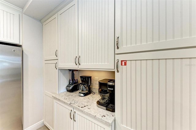 kitchen with light stone countertops, white cabinets, and stainless steel refrigerator