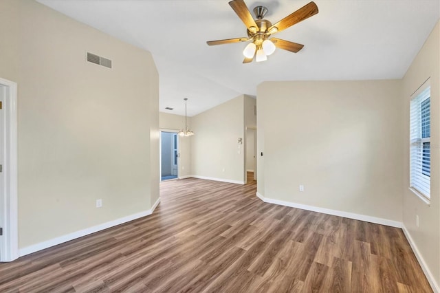 spare room featuring ceiling fan with notable chandelier, dark wood-type flooring, and vaulted ceiling