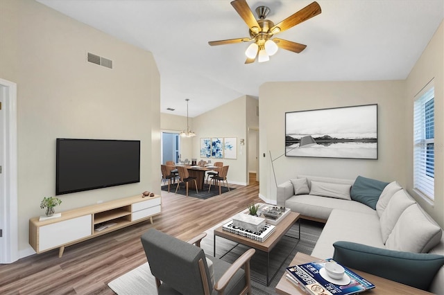 living area with lofted ceiling, ceiling fan with notable chandelier, wood finished floors, and visible vents