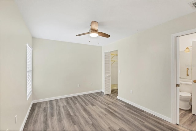 unfurnished bedroom featuring connected bathroom, light wood-style flooring, baseboards, and ceiling fan