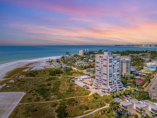 aerial view at dusk featuring a water view and a beach view