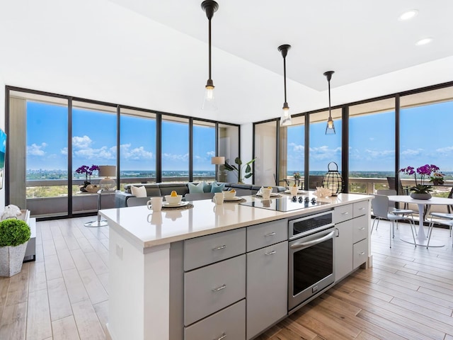 kitchen featuring black electric stovetop, gray cabinetry, stainless steel oven, a kitchen island, and hanging light fixtures