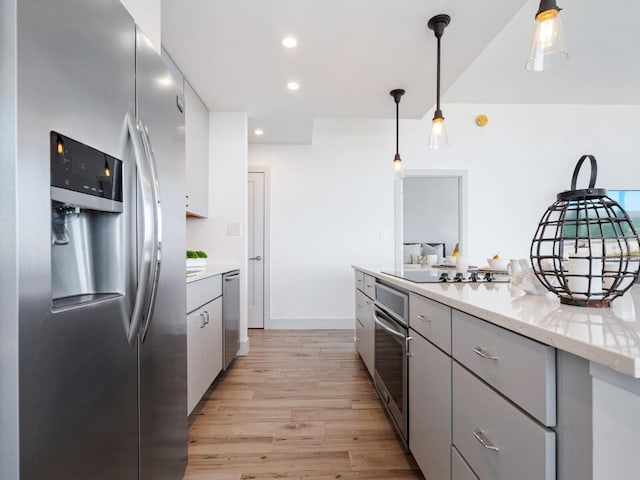 kitchen with stainless steel appliances, light stone counters, pendant lighting, light hardwood / wood-style floors, and gray cabinets