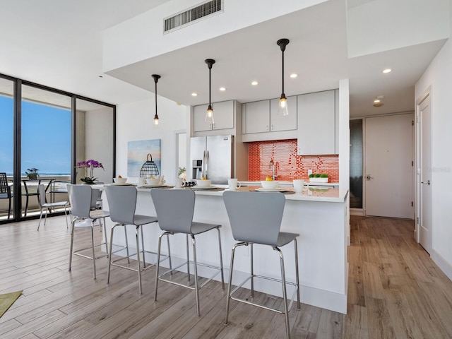 kitchen with tasteful backsplash, floor to ceiling windows, pendant lighting, stainless steel fridge with ice dispenser, and light hardwood / wood-style floors