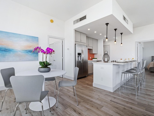 kitchen with stainless steel refrigerator with ice dispenser, backsplash, light hardwood / wood-style flooring, and pendant lighting