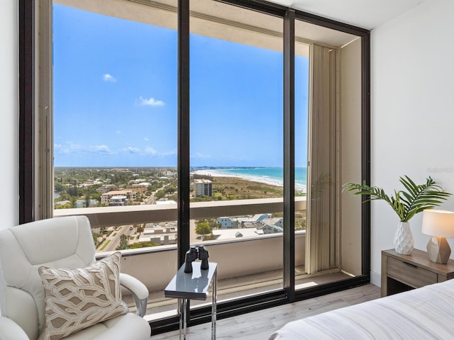 bedroom featuring multiple windows, a water view, a beach view, and light wood-type flooring