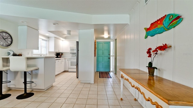 kitchen with white cabinets, white appliances, a breakfast bar area, wooden walls, and light tile patterned floors