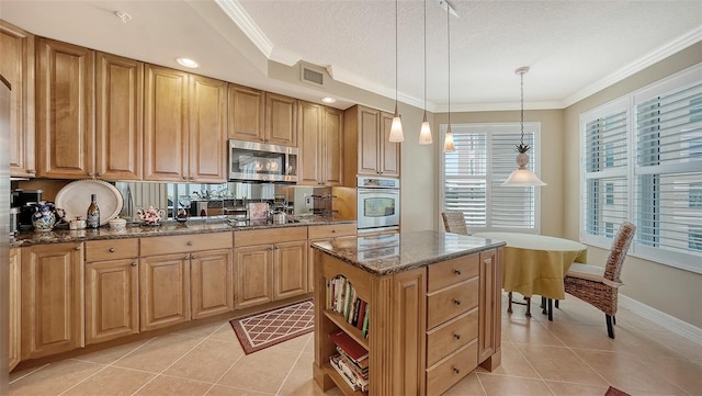 kitchen with appliances with stainless steel finishes, hanging light fixtures, light tile patterned floors, dark stone counters, and ornamental molding