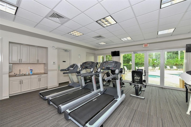 exercise room with a paneled ceiling, carpet flooring, and sink