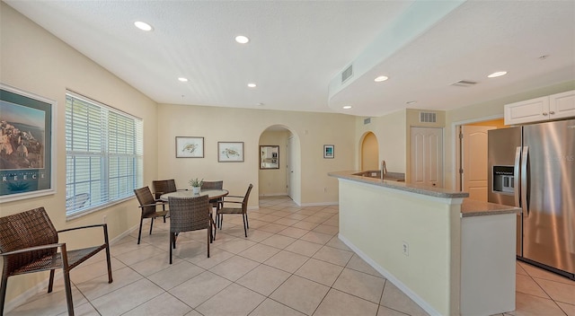 kitchen featuring a kitchen island with sink, stainless steel fridge, white cabinets, and light tile floors