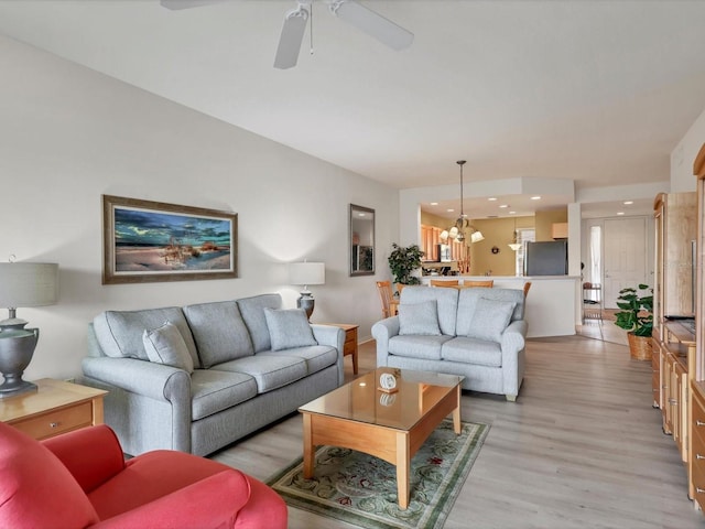 living room with ceiling fan with notable chandelier and light hardwood / wood-style flooring