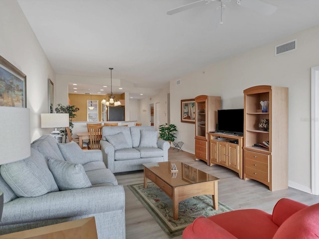 living room featuring ceiling fan with notable chandelier and light wood-type flooring