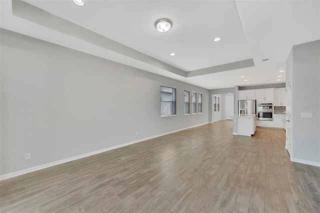 unfurnished living room with a tray ceiling and light wood-type flooring