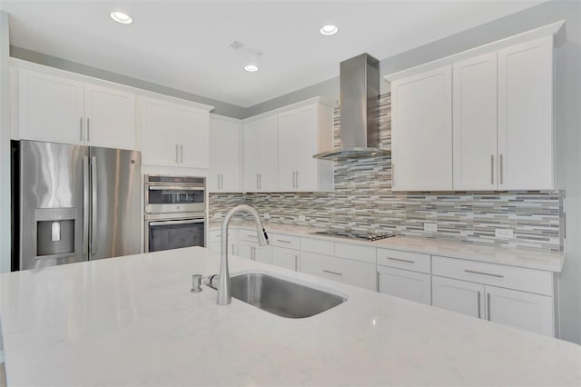 kitchen with white cabinetry, stainless steel appliances, sink, and wall chimney range hood