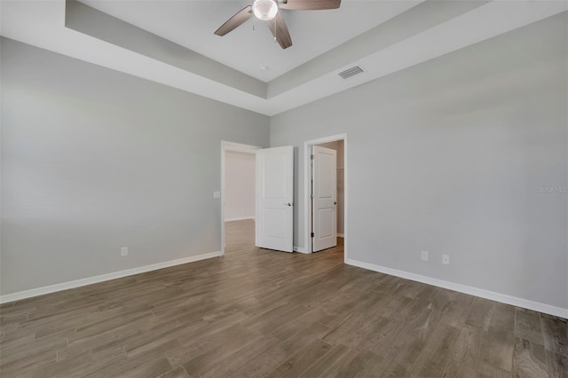 empty room with hardwood / wood-style flooring, a raised ceiling, and ceiling fan