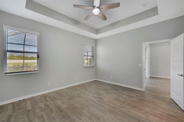 spare room with a tray ceiling, ceiling fan, and light wood-type flooring