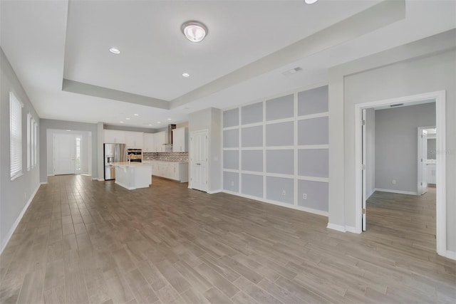 unfurnished living room featuring a tray ceiling and light hardwood / wood-style floors