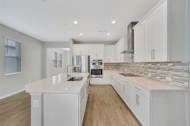 kitchen with sink, appliances with stainless steel finishes, white cabinets, a center island with sink, and wall chimney exhaust hood