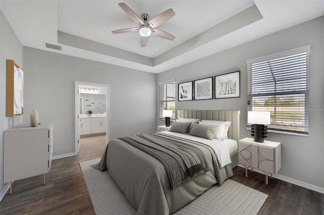 bedroom featuring dark wood-type flooring, connected bathroom, ceiling fan, and a tray ceiling