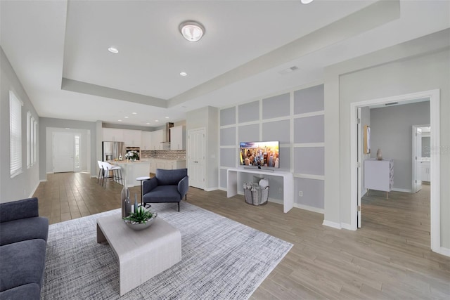 living room with a raised ceiling and light wood-type flooring