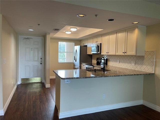 kitchen with dark wood-type flooring, appliances with stainless steel finishes, white cabinets, kitchen peninsula, and backsplash