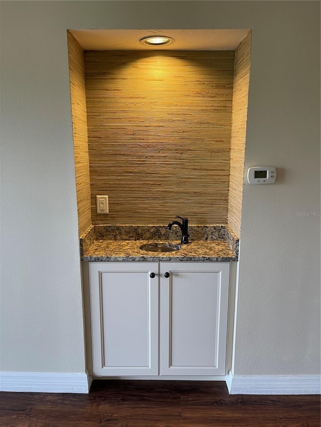 bar with white cabinetry, sink, dark stone countertops, and dark wood-type flooring