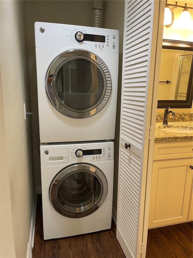 laundry room featuring sink, dark wood-type flooring, and stacked washer / drying machine