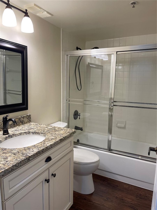 full bathroom with enclosed tub / shower combo, vanity with extensive cabinet space, toilet, and hardwood / wood-style floors