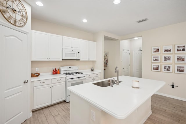 kitchen with white appliances, a center island with sink, white cabinets, sink, and light hardwood / wood-style flooring