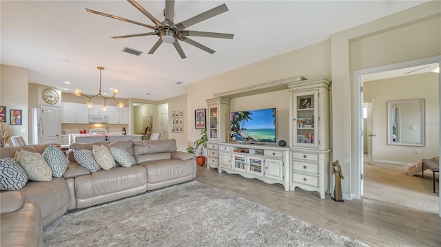 living room with ceiling fan with notable chandelier and light hardwood / wood-style floors