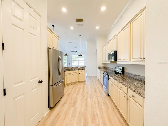 kitchen featuring stainless steel appliances, cream cabinetry, dark stone counters, light wood finished floors, and pendant lighting