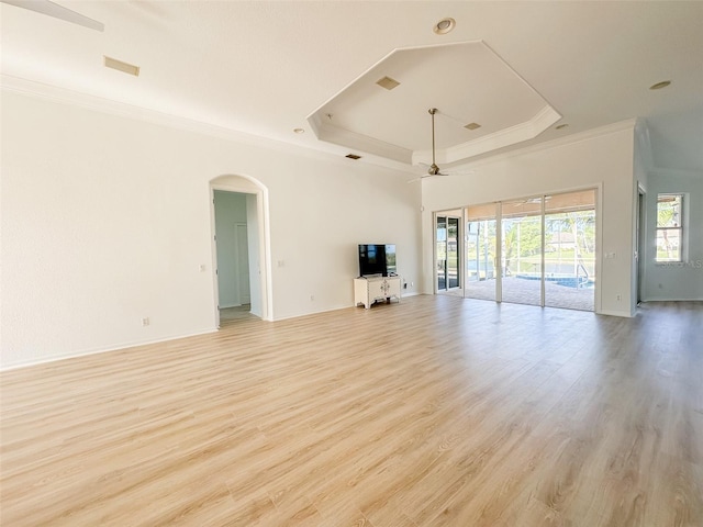 unfurnished living room with arched walkways, a raised ceiling, light wood-style flooring, and crown molding