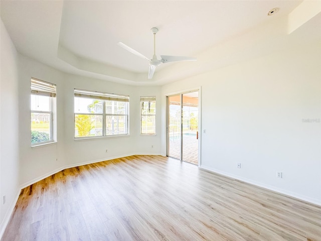 unfurnished room with light wood-type flooring, a tray ceiling, a healthy amount of sunlight, and baseboards