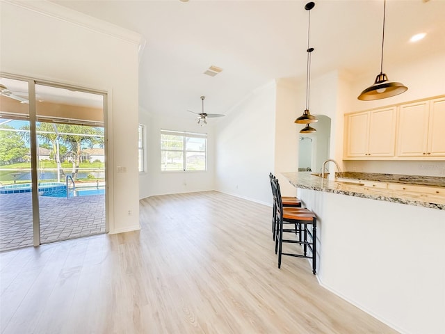 kitchen with light stone counters, pendant lighting, light wood finished floors, and a ceiling fan