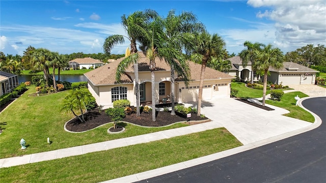 mediterranean / spanish house featuring stucco siding, concrete driveway, a water view, an attached garage, and a front lawn