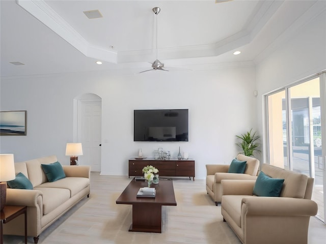 living area with arched walkways, ornamental molding, a raised ceiling, and recessed lighting