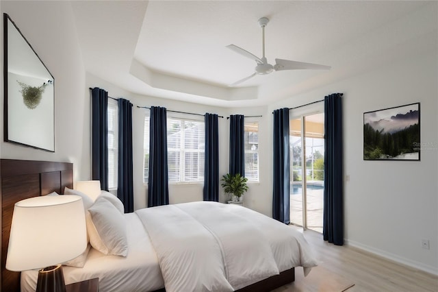 bedroom with a ceiling fan, baseboards, access to exterior, light wood finished floors, and a raised ceiling