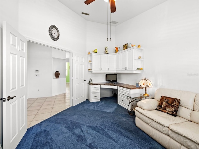 office featuring ceiling fan, a towering ceiling, built in desk, and light colored carpet