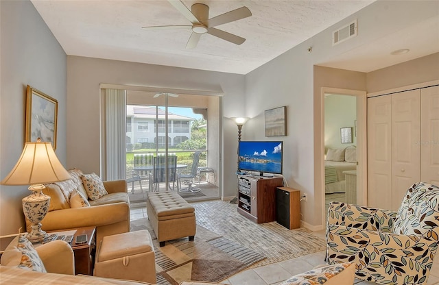 living room featuring ceiling fan, a textured ceiling, and light tile patterned floors