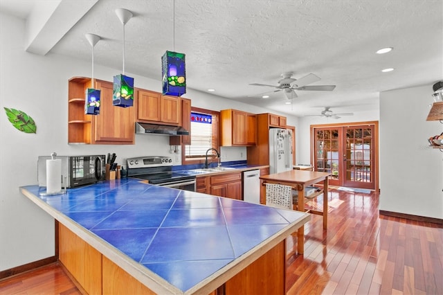 kitchen featuring kitchen peninsula, light hardwood / wood-style flooring, appliances with stainless steel finishes, decorative light fixtures, and sink