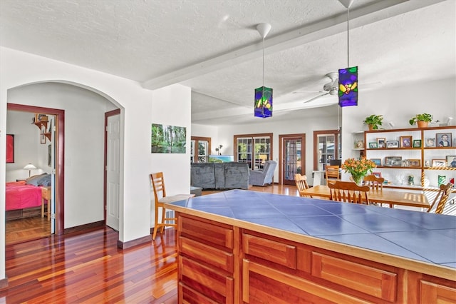 kitchen with beam ceiling, hardwood / wood-style floors, tile counters, and a textured ceiling