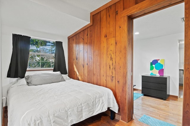 bedroom with light hardwood / wood-style floors, wooden walls, and a closet